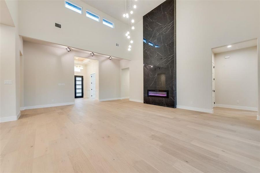Unfurnished living room with a high ceiling, healthy amount of natural light, light wood-style flooring, a fireplace, and baseboards Unfurnished living room with a high ceiling, healthy amount of natural light, light wood-style flooring, a fireplace, and baseboards