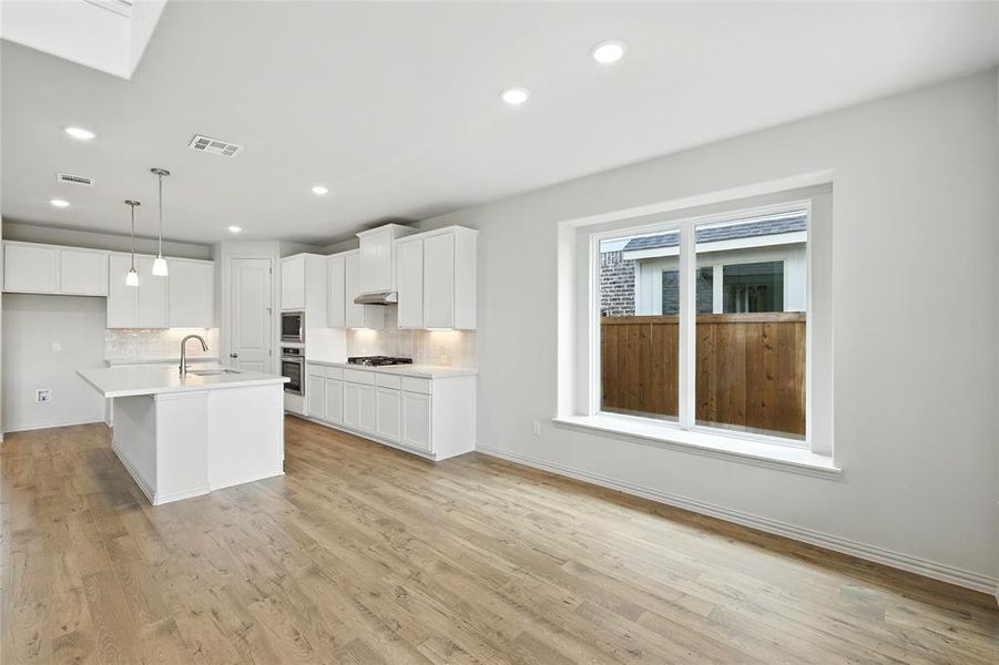 Kitchen featuring tasteful backsplash, an island with sink, light wood finished floors, hanging light fixtures, and recessed lighting