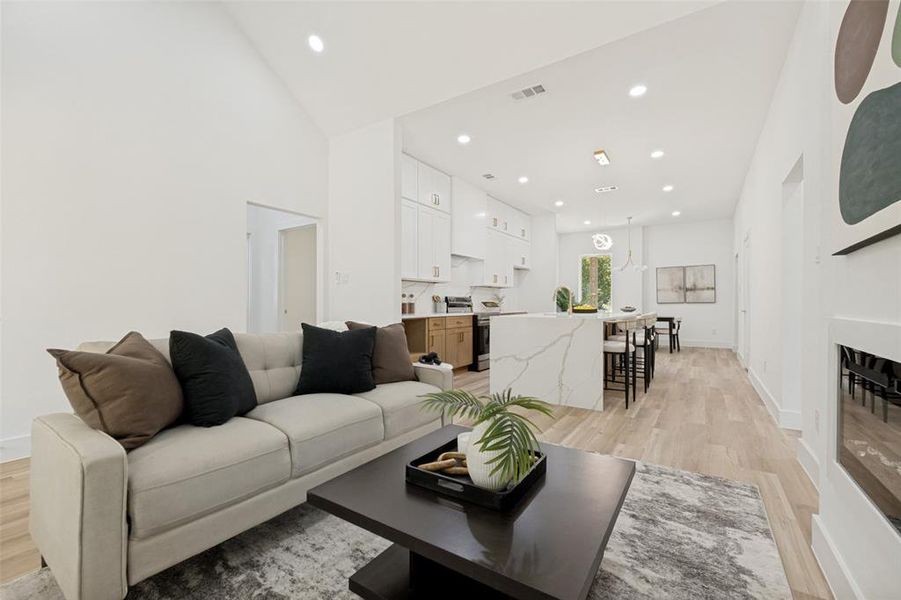 Spacious open-concept living area featuring high vaulted ceilings, light wood-finish flooring, recessed lighting, and a modern built-in fireplace Spacious open-concept living area featuring high vaulted ceilings, light wood-finish flooring, recessed lighting, and a modern built-in fireplace