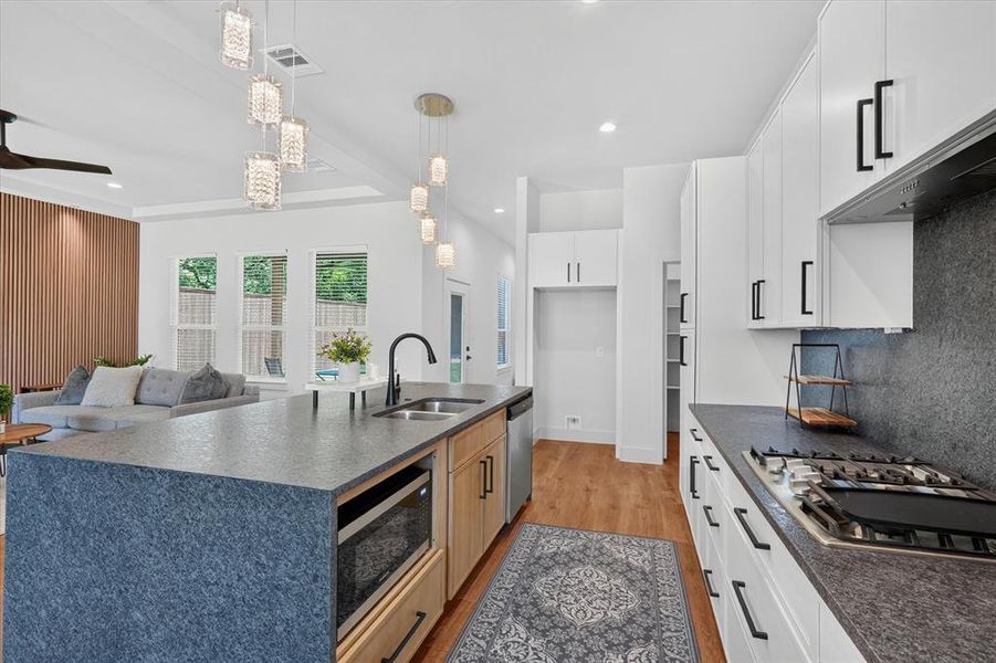 Open-concept kitchen featuring an oversized island with an undermount sink, built-in microwave, and wood-finish cabinetry