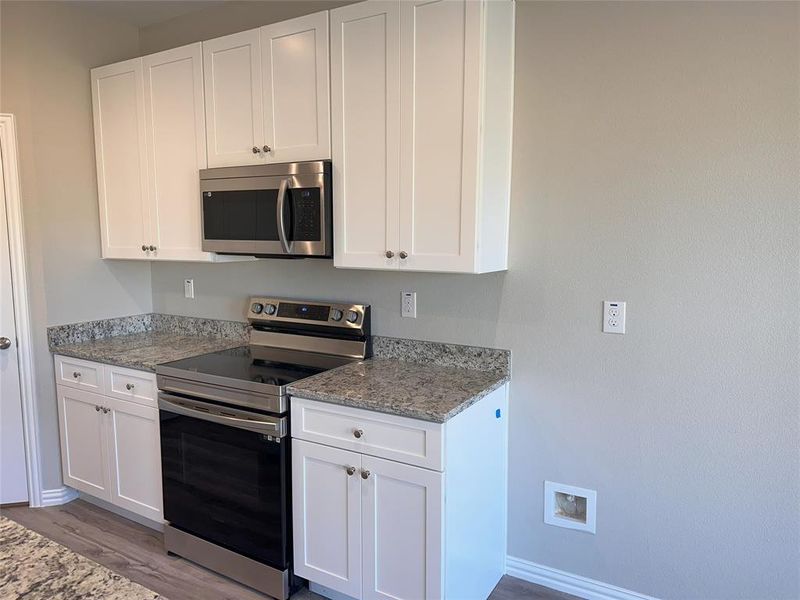 Kitchen featuring stainless steel appliances, light stone counters, white cabinets, and light hardwood / wood-style floors