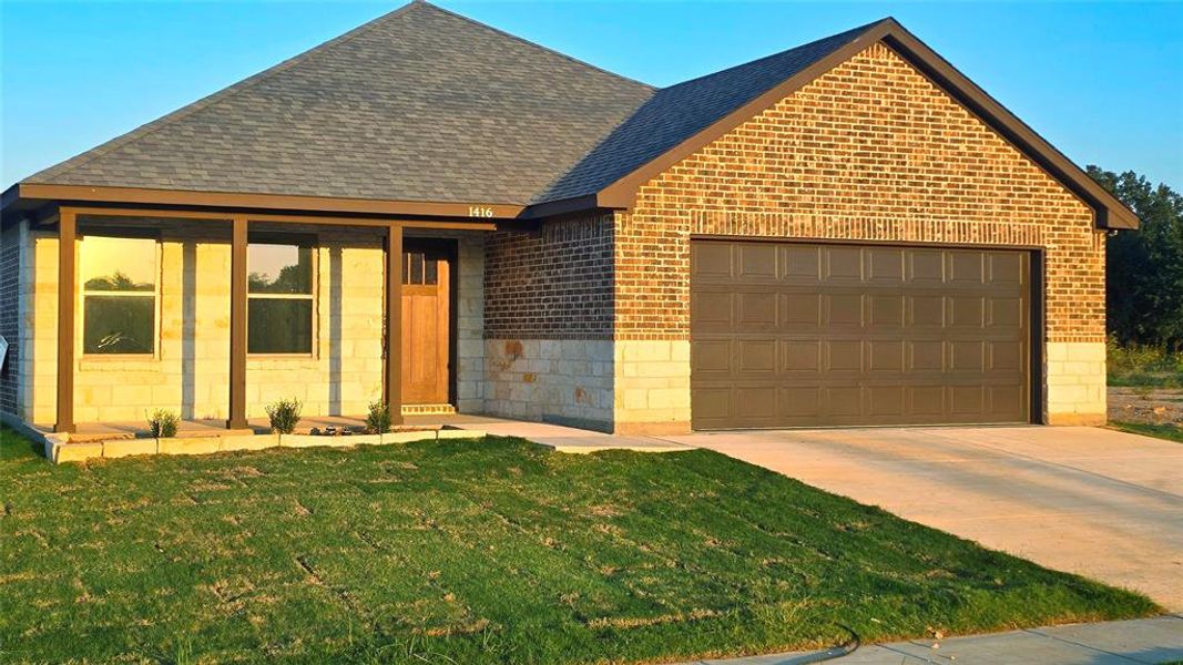 View of front of home featuring roof with shingles, a front lawn, a garage, brick siding, and driveway