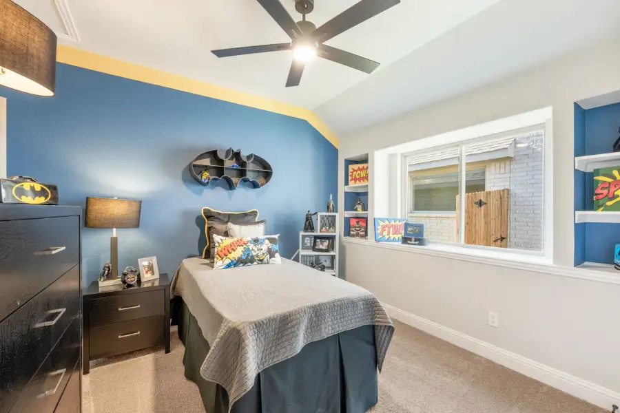 Kids' bedroom with blue walls, Batman-themed decor, ceiling fan, and carpeted floor