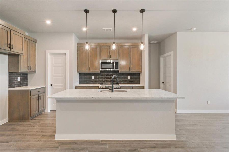 Kitchen with hanging light fixtures, light stone counters, tasteful backsplash, stainless steel microwave, and recessed lighting