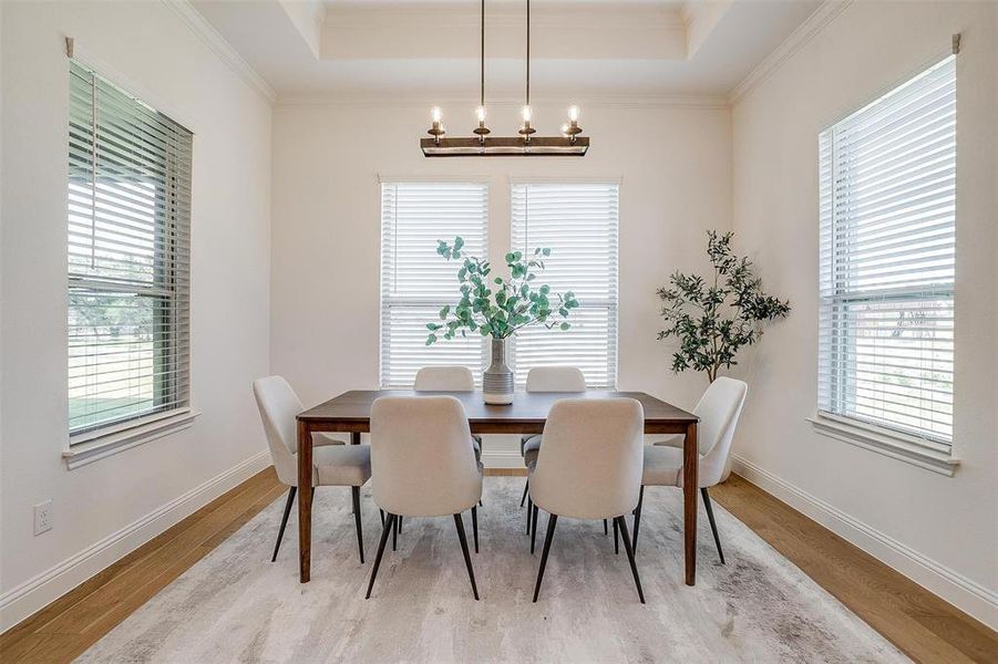 Dining area with an inviting chandelier, crown molding, a tray ceiling, and light hardwood / wood-style floors