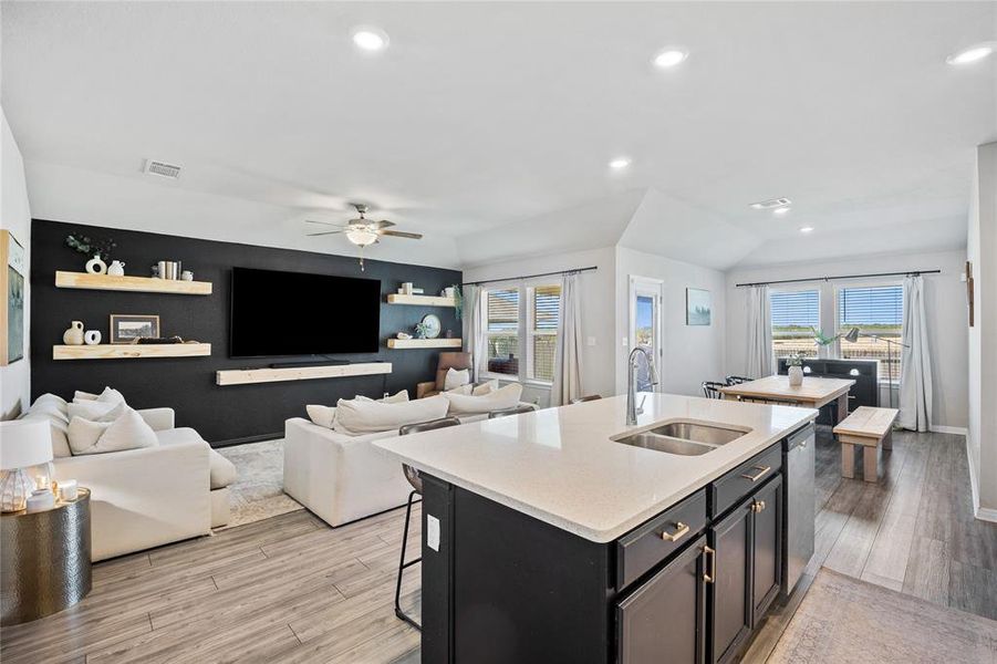 Kitchen featuring dark cabinets, open floor plan, light wood-style flooring, light stone counters, and recessed lighting