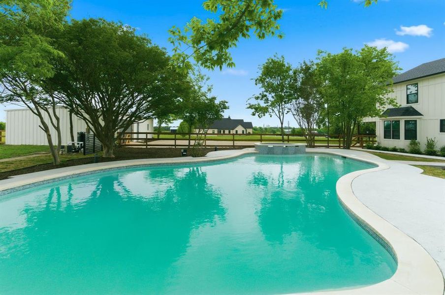 The property features a large, irregularly shaped swimming pool with a light-colored pool deck and a raised spa area The property features a large, irregularly shaped swimming pool with a light-colored pool deck and a raised spa area