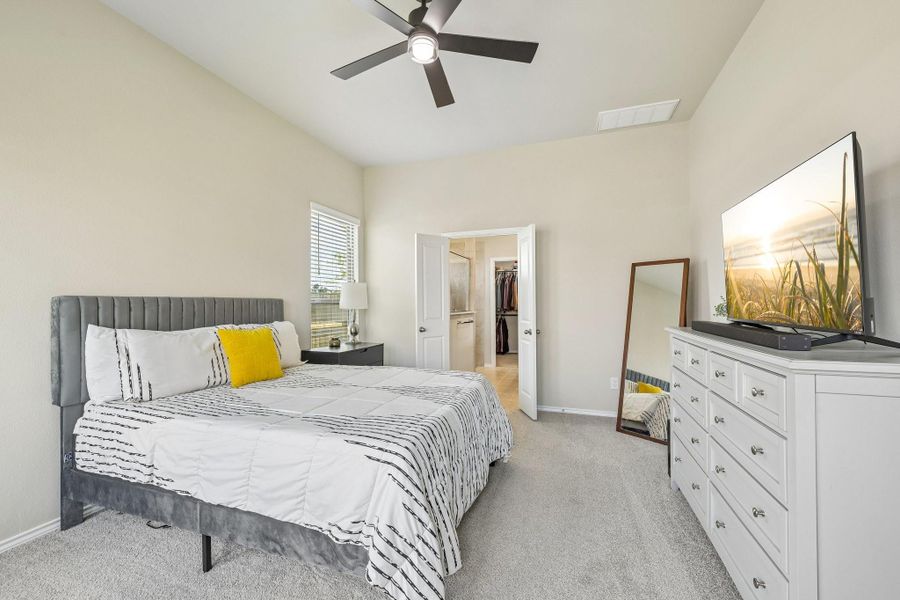 Spacious bedroom with a modern ceiling fan, plush carpeting, and ample natural light, featuring a walk-in closet and stylish decor.