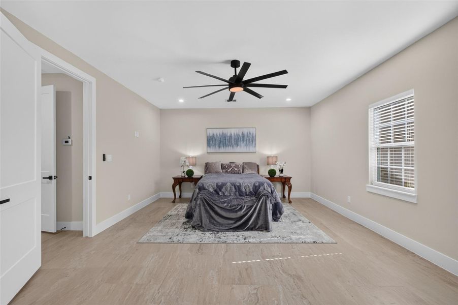 Spacious bedroom featuring a modern ceiling fan, large window for natural light, and elegant wood flooring.