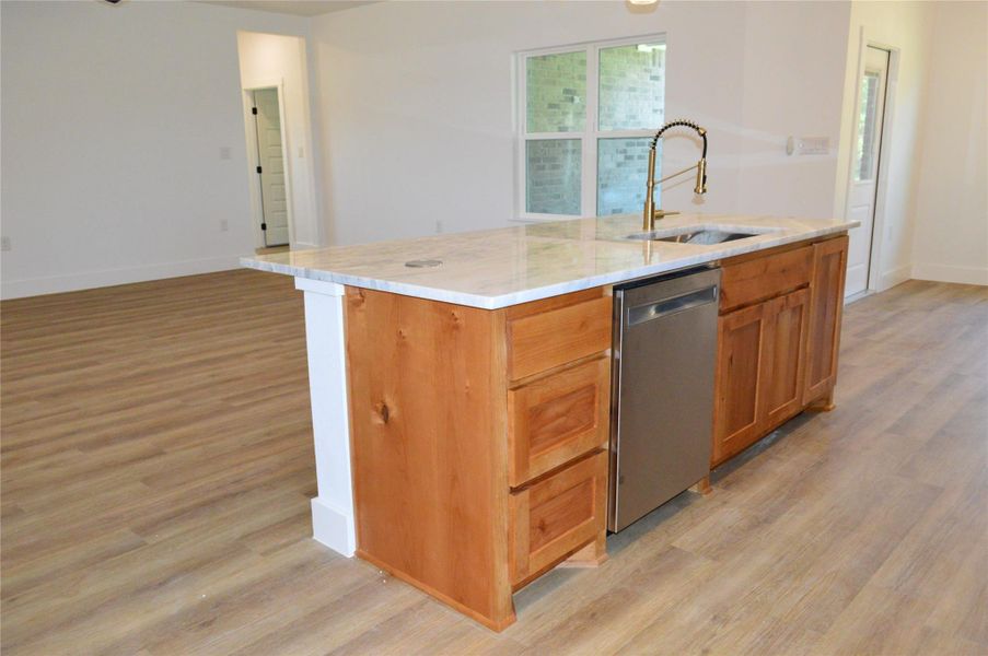 Kitchen featuring brown cabinets, dishwasher, light stone counters, an island with sink, and light wood-style flooring Kitchen featuring brown cabinets, dishwasher, light stone counters, an island with sink, and light wood-style flooring