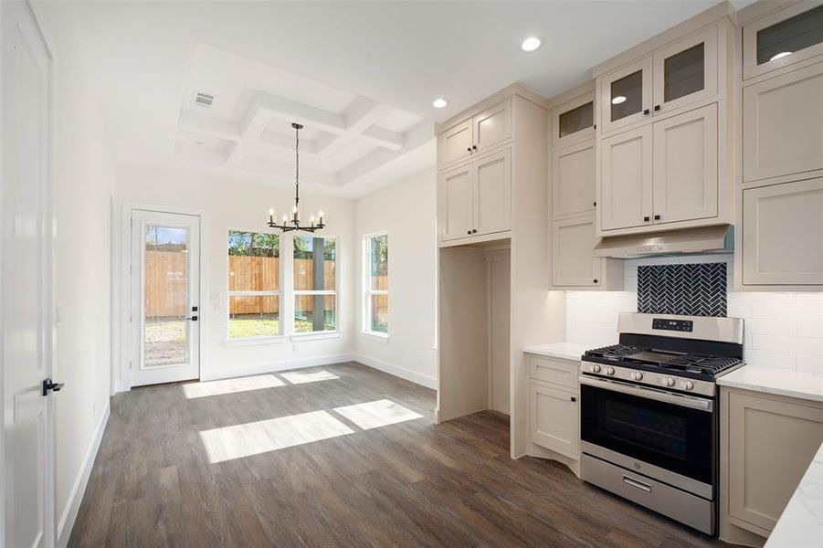 Kitchen with stainless steel range with gas cooktop, coffered ceiling, dark wood finished floors, tasteful backsplash, and decorative light fixtures Kitchen with stainless steel range with gas cooktop, coffered ceiling, dark wood finished floors, tasteful backsplash, and decorative light fixtures