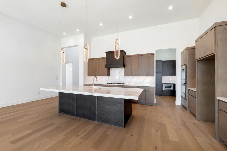 Kitchen with a large island with sink, light stone countertops, modern cabinets, pendant lighting, and light wood-type flooring