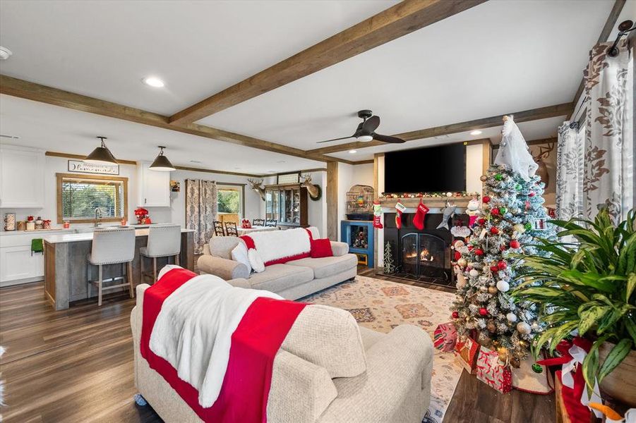 Open-concept living area with wood-finish flooring, exposed ceiling beams, a built-in fireplace, and a kitchen island with seating