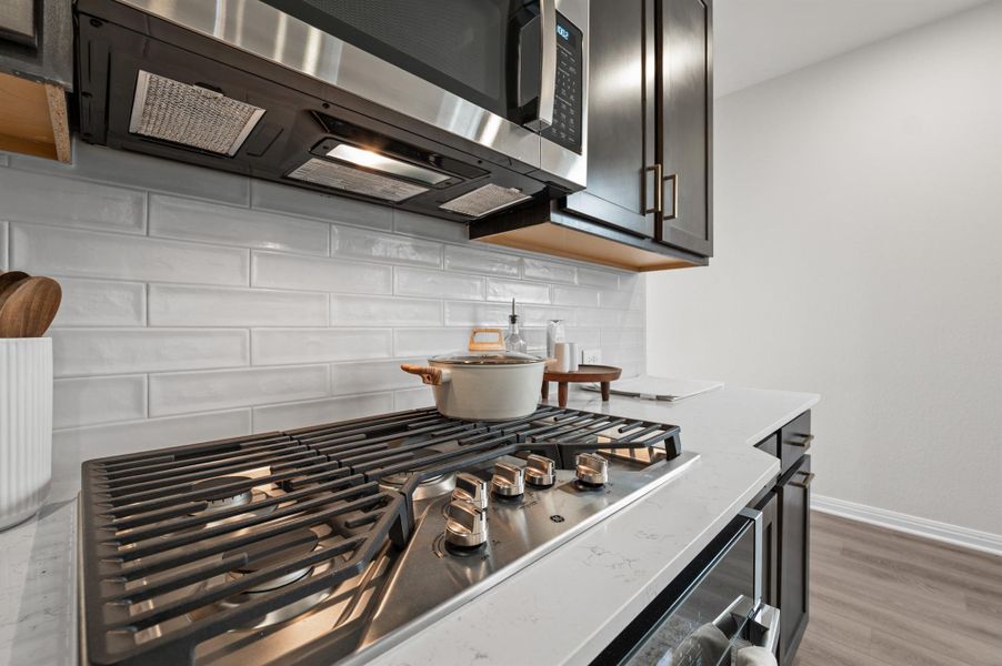Kitchen view of stainless steel appliances, tasteful backsplash, light wood-style flooring, and light stone counters Kitchen view of stainless steel appliances, tasteful backsplash, light wood-style flooring, and light stone counters