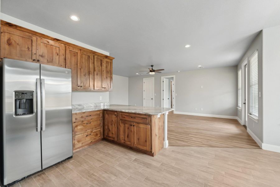 Kitchen featuring light stone counters, a peninsula, light wood-style flooring, ceiling fan, and stainless steel fridge