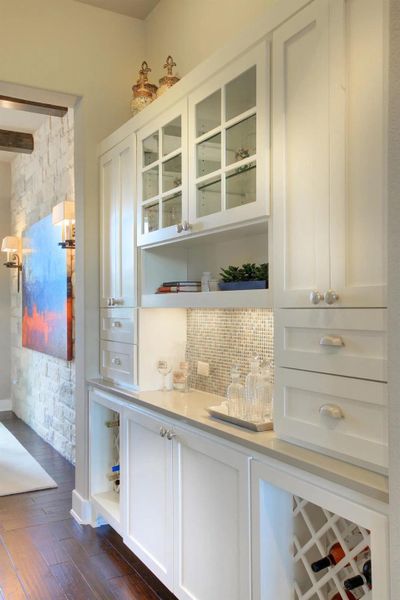 Bar area with white cabinets, open shelves, glass insert cabinets, and dark wood-style flooring Bar area with white cabinets, open shelves, glass insert cabinets, and dark wood-style flooring