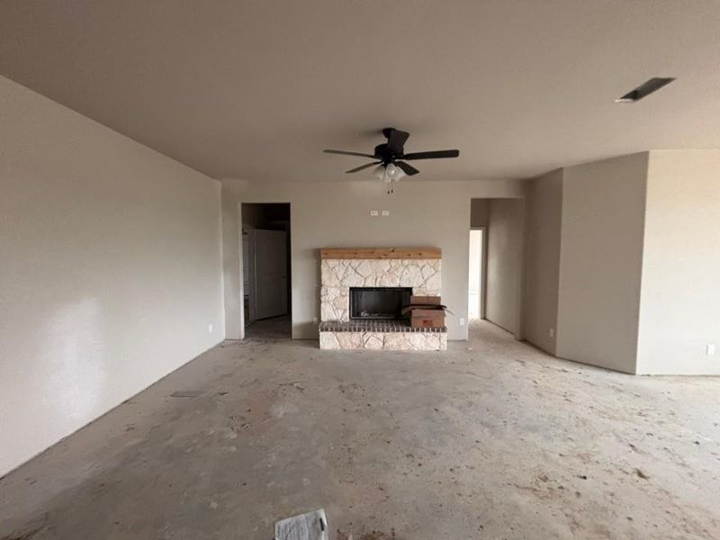 Living space featuring a stone-faced fireplace with a wood mantel, a ceiling fan with integrated lighting, and neutral wall tones