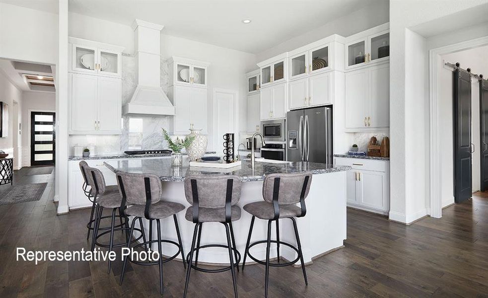 Kitchen featuring a large central island with seating, white cabinetry with glass-front uppers, stainless steel appliances, and wood-finish flooring