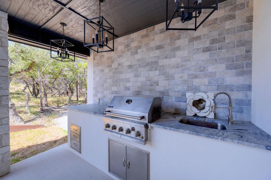 A stone accent wall and granite countertops anchor this covered outdoor kitchen space.
