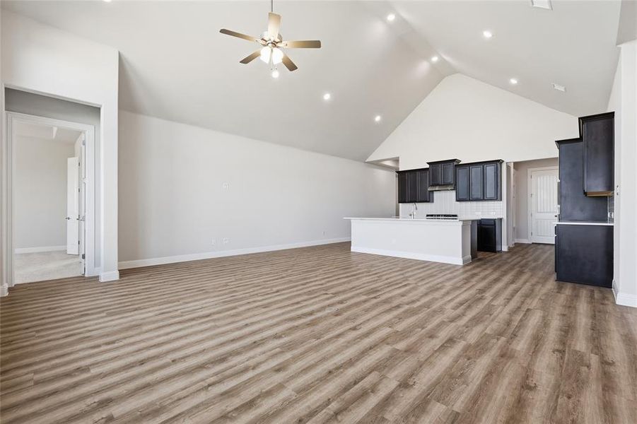 Unfurnished living room featuring a high ceiling, a ceiling fan, light wood finished floors, and recessed lighting Unfurnished living room featuring a high ceiling, a ceiling fan, light wood finished floors, and recessed lighting