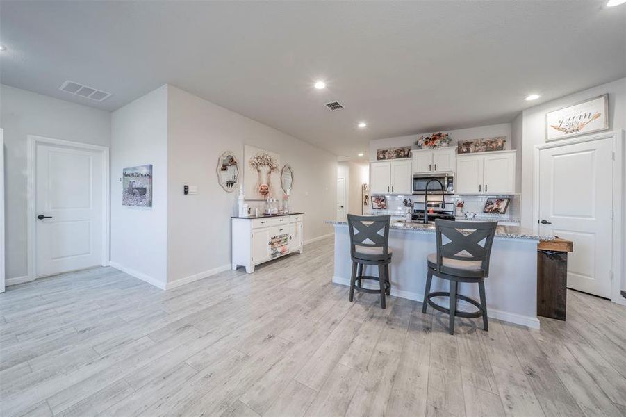 Kitchen with appliances with stainless steel finishes, light wood-type flooring, a center island with sink, white cabinets, and a breakfast bar area