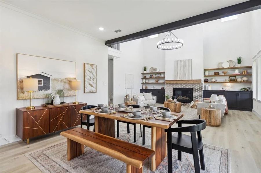 Dining area with light wood-type flooring, a brick fireplace, suspended lighting, a high ceiling, and ornamental molding