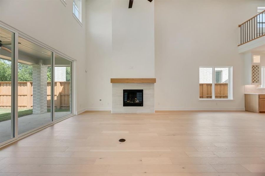Unfurnished living room featuring a high ceiling, a ceiling fan, light wood finished floors, and a fireplace Unfurnished living room featuring a high ceiling, a ceiling fan, light wood finished floors, and a fireplace