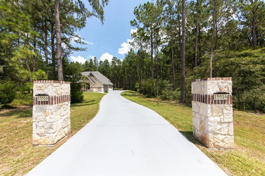 This photo shows a serene property with a long driveway flanked by stone pillars, leading through a wooded area to a charming home. The setting offers privacy and a natural landscape, ideal for those seeking a peaceful retreat.