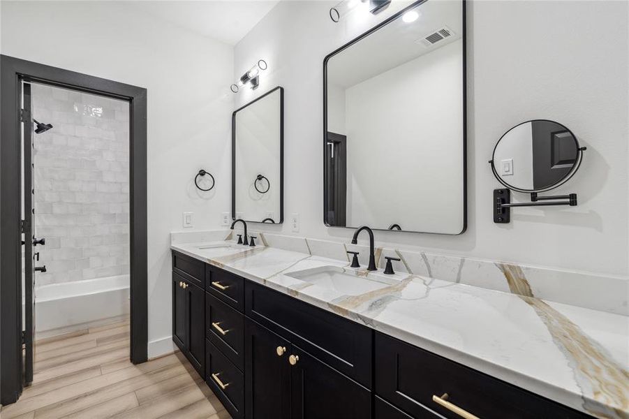 This secondary bathroom features a double vanity with ample counter and cabinet space, while the striking black wood trim and matte black fixtures add a bold, modern touch.