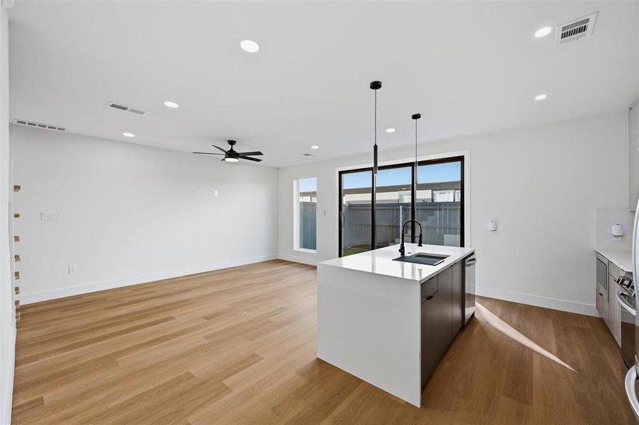 Living Room features recessed lighting and ceiling fan with light fixture. Large window and sliding glass door provide abundant natural light and backyard views. Open-concept layout connects directly to the kitchen island. Vinyl flooring extends throughout.