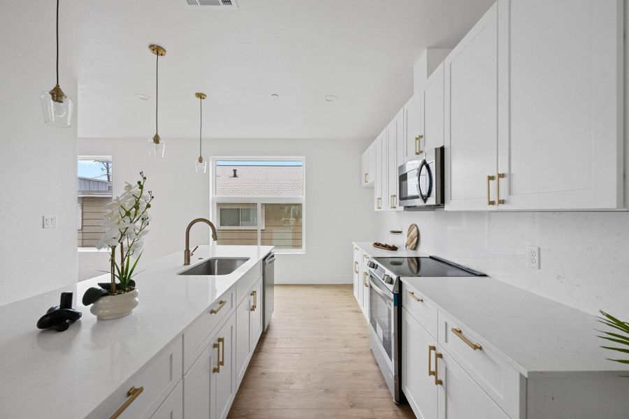 Modern kitchen featuring extensive white cabinetry with gold-finish hardware, stainless steel appliances, a large center island with an undermount sink, and wood-finish flooring