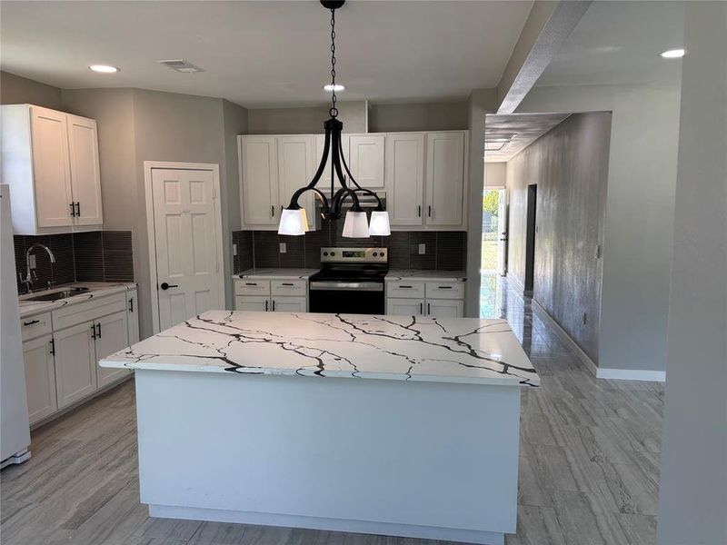 Kitchen with hanging light fixtures, electric range, decorative backsplash, white cabinets, and light wood-style floors Kitchen with hanging light fixtures, electric range, decorative backsplash, white cabinets, and light wood-style floors