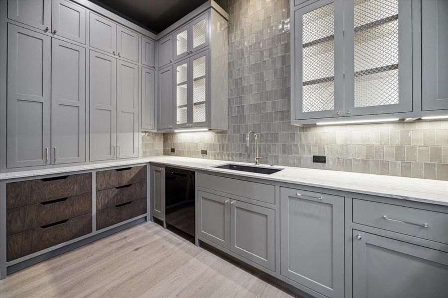 A luxurious pantry/butler’s pantry offers additional storage with custom cabinetry and a stylish tiled backsplash. Complete with additional sink, second dishwasher, a wine fridge, and plenty of counter space for prep work or serving.