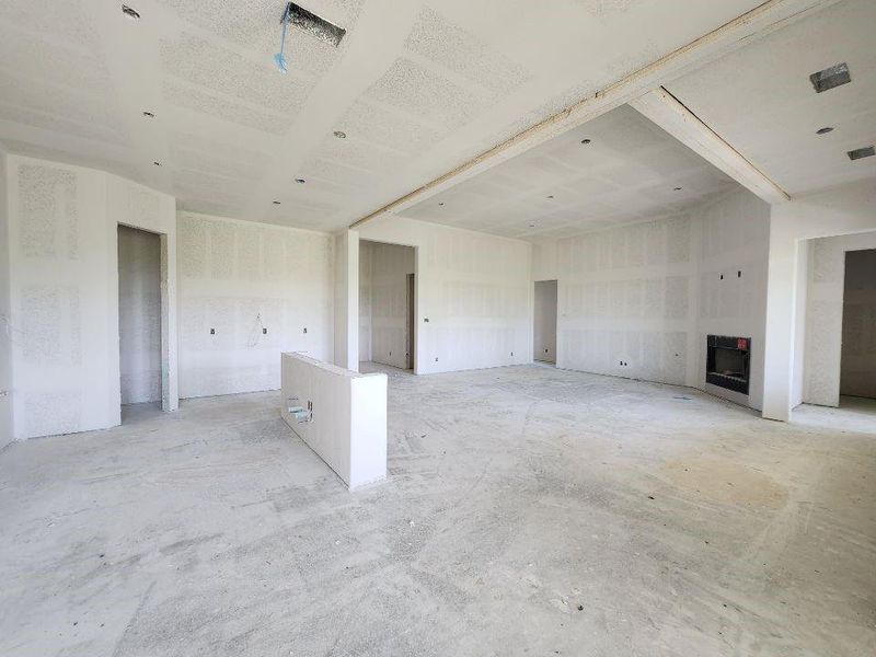Open-concept interior space under construction, featuring a built-in fireplace, recessed ceiling lighting, and a partially framed island