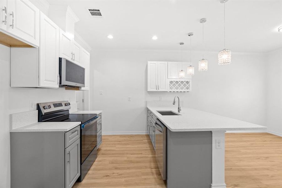 Kitchen with stainless steel appliances, a peninsula, light wood finished floors, crown molding, and light countertops Kitchen with stainless steel appliances, a peninsula, light wood finished floors, crown molding, and light countertops