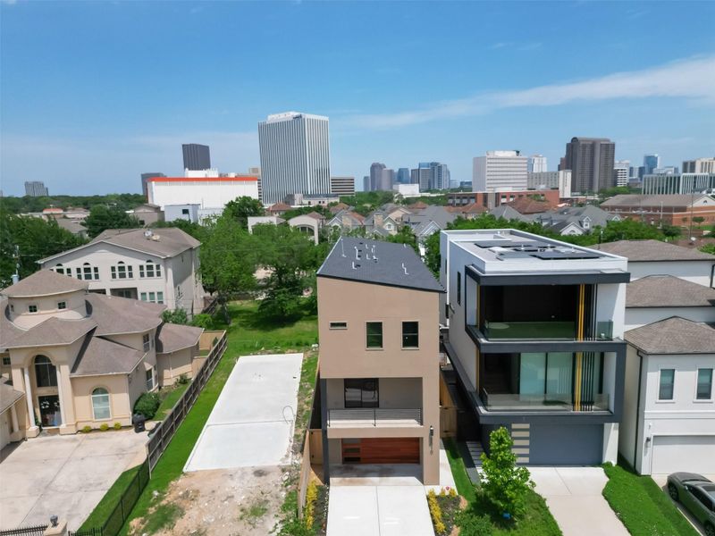 This is an aerial view of a contemporary, multi-story home with a flat roof, large windows, and a mix of grey and wood exterior finishes. The property includes a driveway, and it's located in a residential area with similar upscale homes, near a city skyline suggesting close proximity to urban amenities. This is an aerial view of a contemporary, multi-story home with a flat roof, large windows, and a mix of grey and wood exterior finishes. The property includes a driveway, and it's located in a residential area with similar upscale homes, near a city skyline suggesting close proximity to urban amenities.