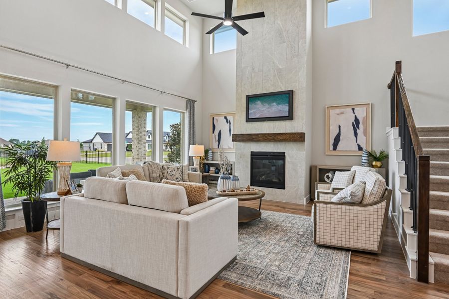 Open living room with two-story ceiling, stone fireplace, hardwood floors, and large windows with backyard view