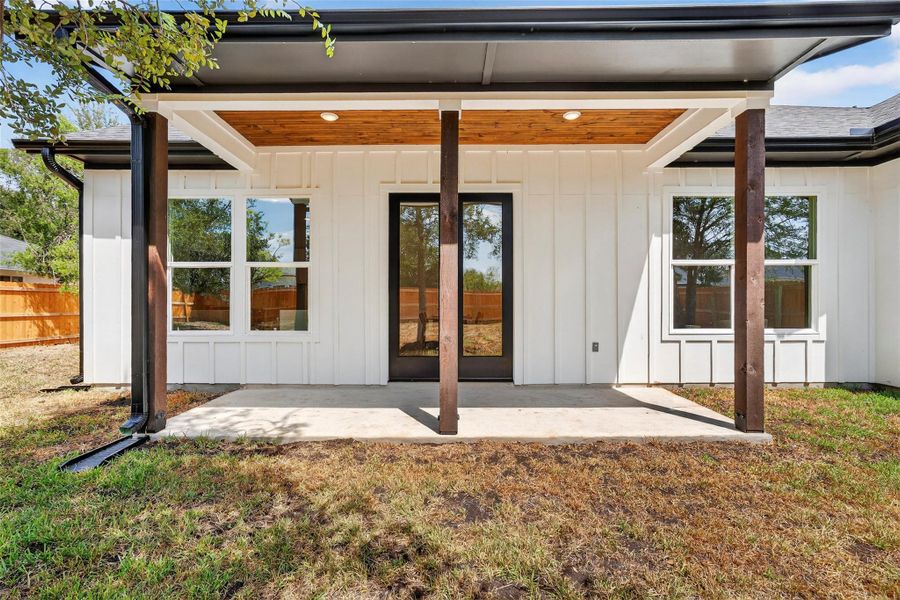 Entrance to property featuring board and batten siding, a patio, and a lawn