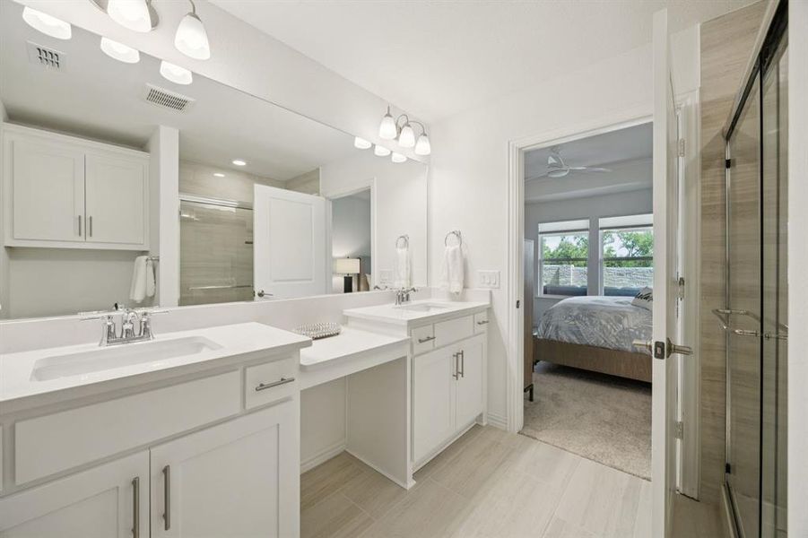 The spacious primary bathroom provides dual vanities with the make-up vanity in between. The vanity is quartz and features undermount wave sinks. The flooring is tile.