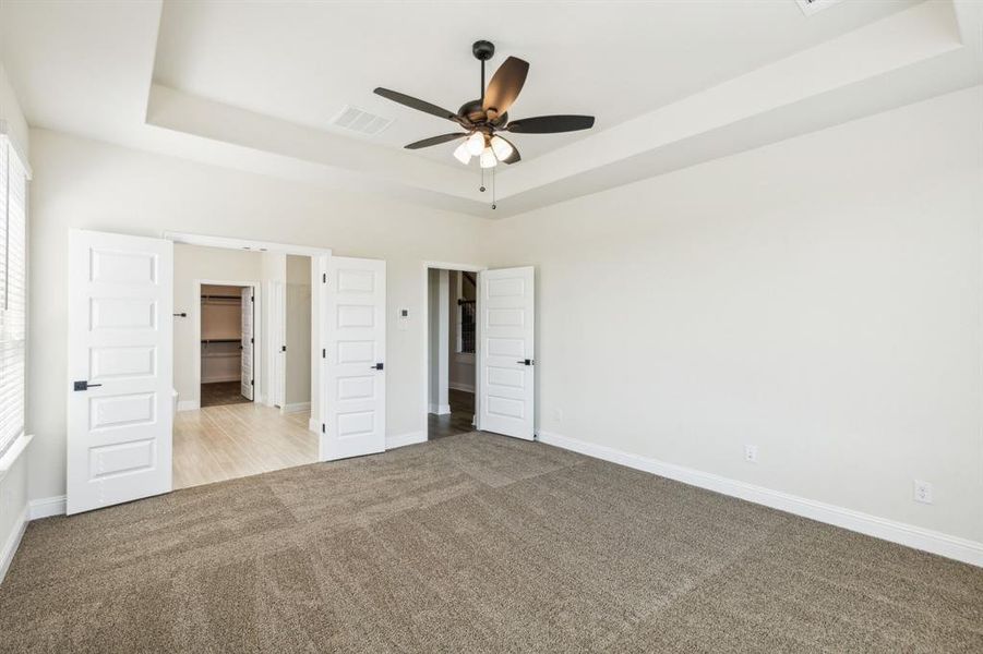 Unfurnished bedroom with ceiling fan, light carpet, and a tray ceiling