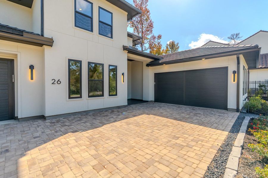 Modern home with a sleek design, featuring a spacious two-car garage and a beautifully paved driveway. The exterior is complemented by stylish lighting and well-maintained landscaping, creating an inviting entrance.