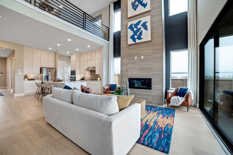 Living room with light wood-style floors, a tiled fireplace, healthy amount of natural light, a high ceiling, and recessed lighting