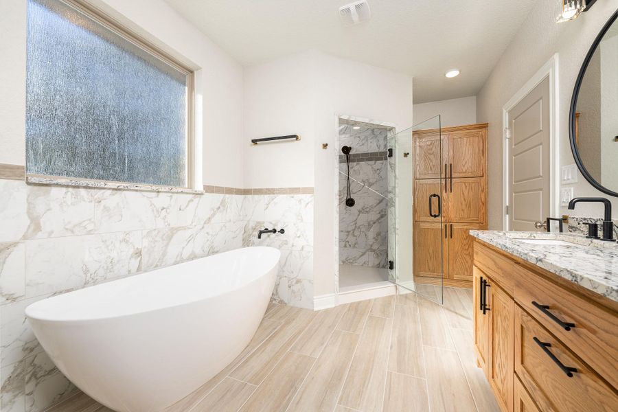 Bathroom featuring a freestanding tub, a marble finish shower, vanity, tile walls, and wainscoting Bathroom featuring a freestanding tub, a marble finish shower, vanity, tile walls, and wainscoting
