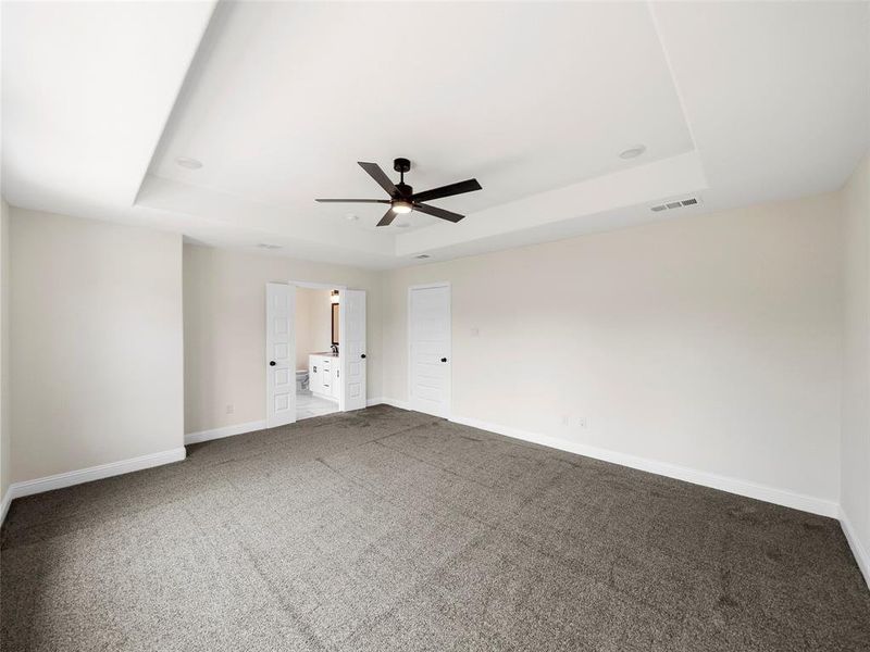 Carpeted empty room featuring ceiling fan and a tray ceiling