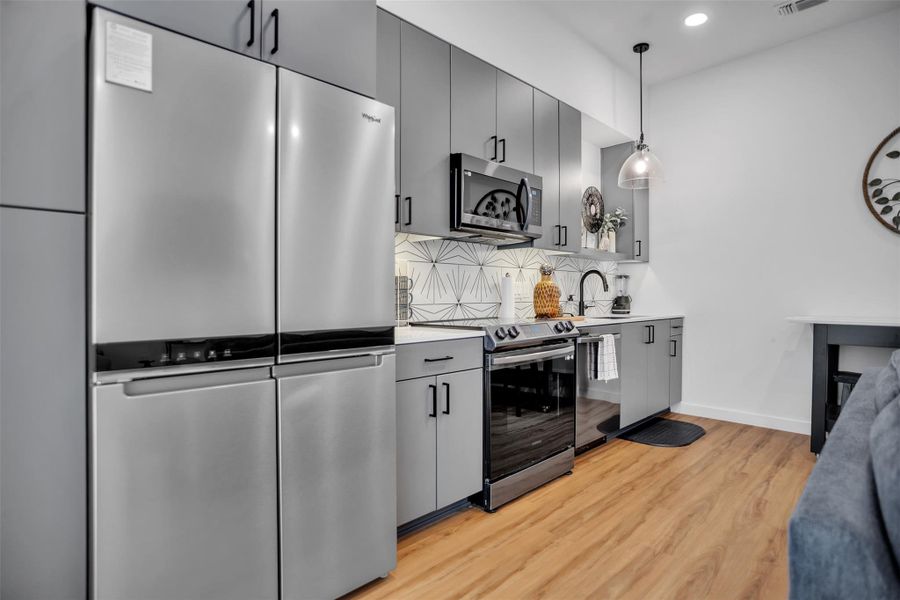 Kitchen with decorative light fixtures, stainless steel appliances, tasteful backsplash, light wood-style flooring, and a sink