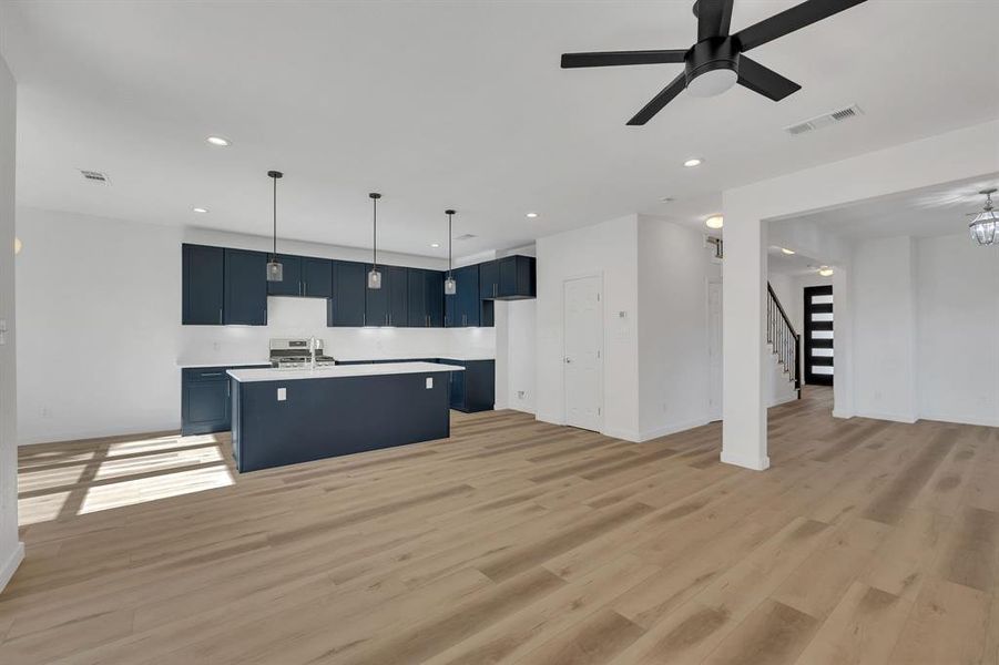 Kitchen with open floor plan, a kitchen island with sink, hanging light fixtures, light wood-style floors, and recessed lighting