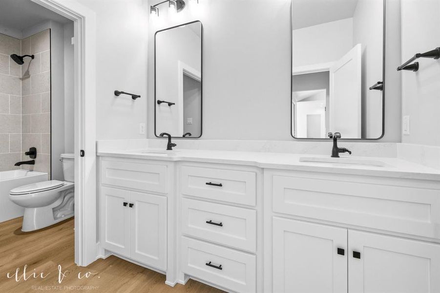 Full bath featuring shower / washtub combination, double vanity, and light wood-style floors