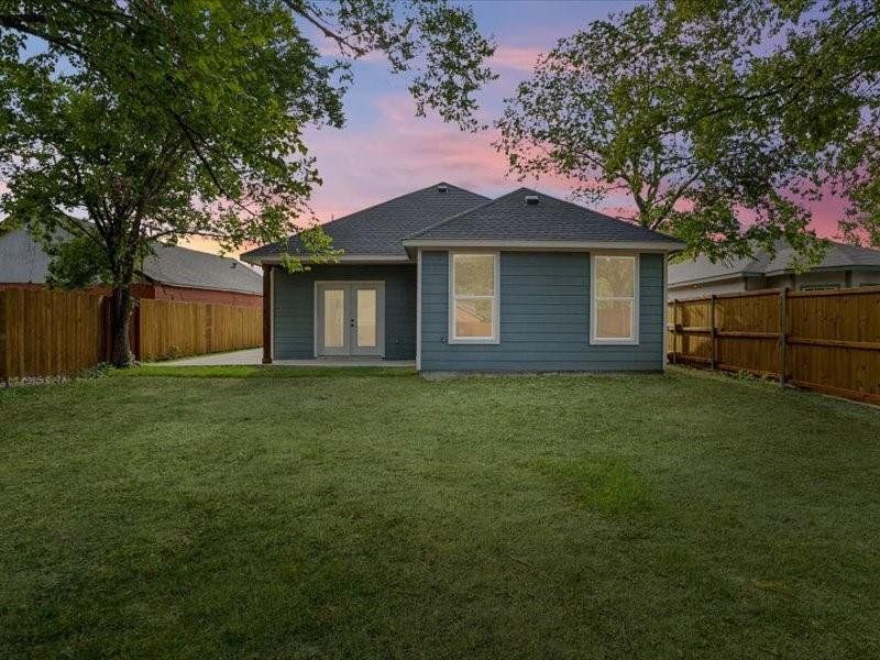 Back house at dusk featuring french doors and a lawn