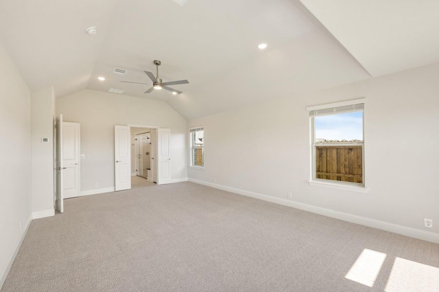 Spacious bedroom with vaulted ceiling, ceiling fan, carpet flooring, and open ensuite bathroom door. Spacious bedroom with vaulted ceiling, ceiling fan, carpet flooring, and open ensuite bathroom door.