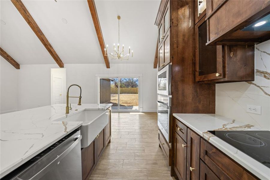 Kitchen featuring dark wood finish cabinetry, range hood, lofted ceiling with beams, stainless steel appliances, and light stone countertops